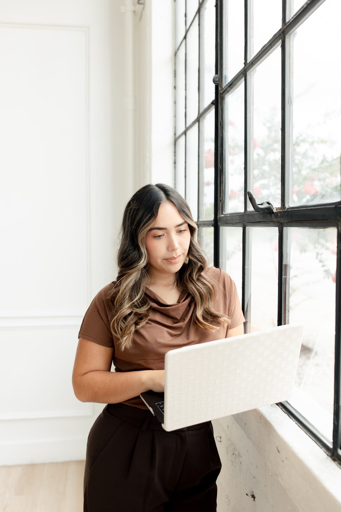 Valeria working on a laptop beside a large studio window